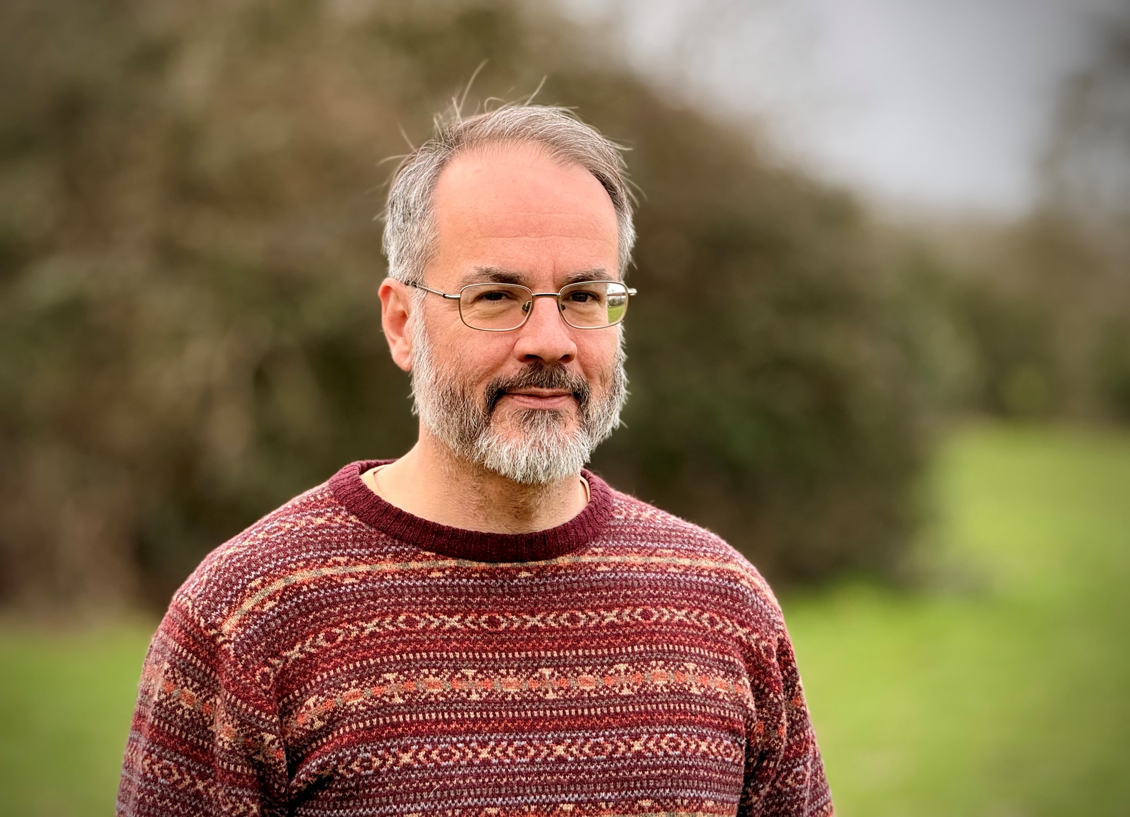 Man with glasses and beard in patterned sweater outdoors