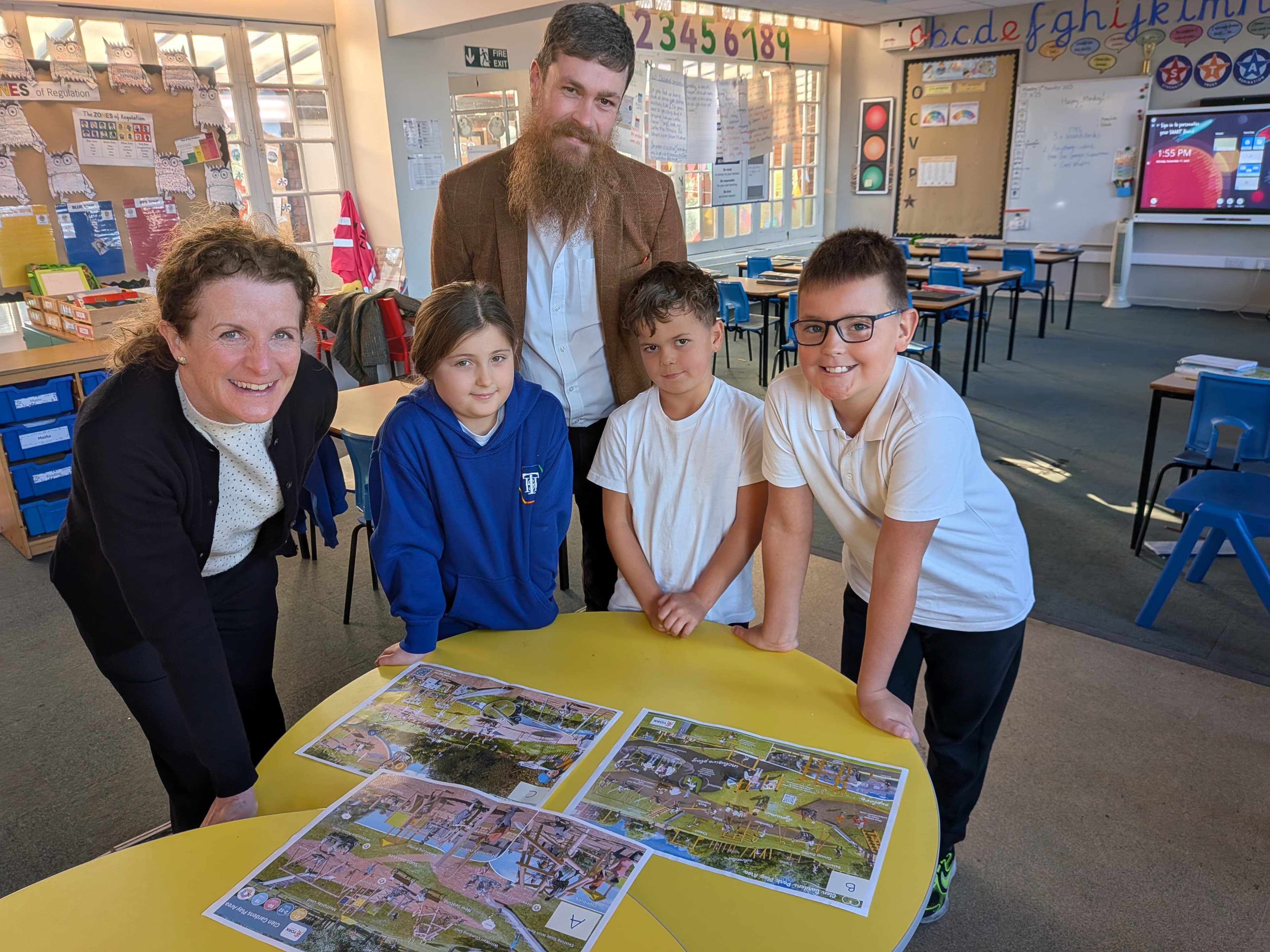 Schoolchildren and teachers examining maps on classroom table