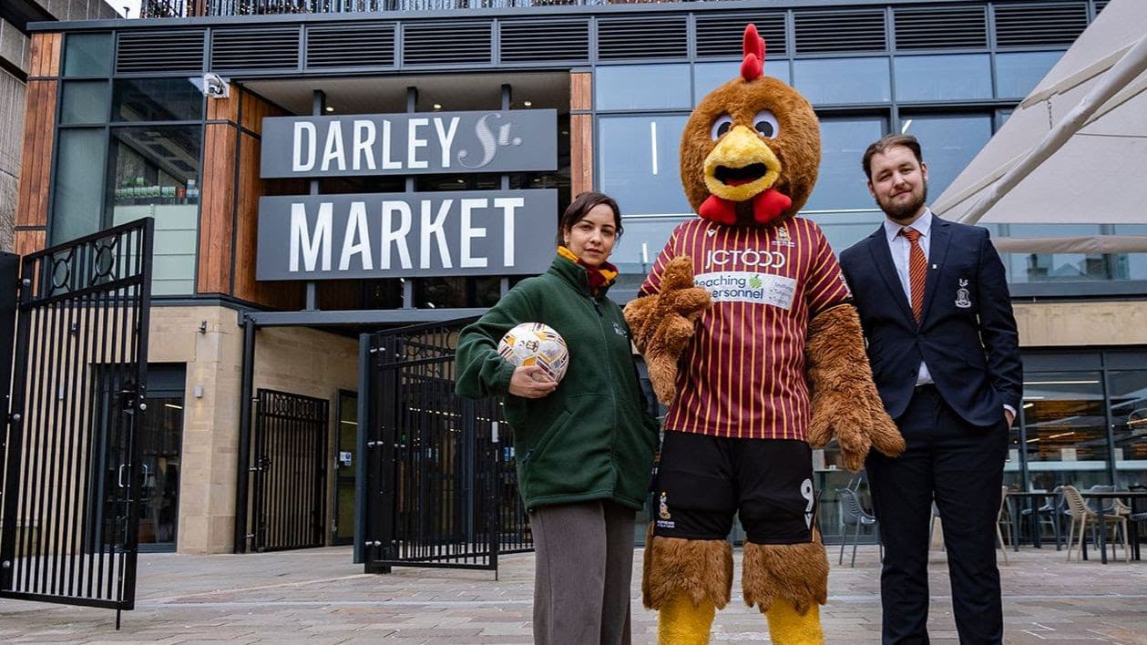 Three people, including a mascot, outside Darley St Market