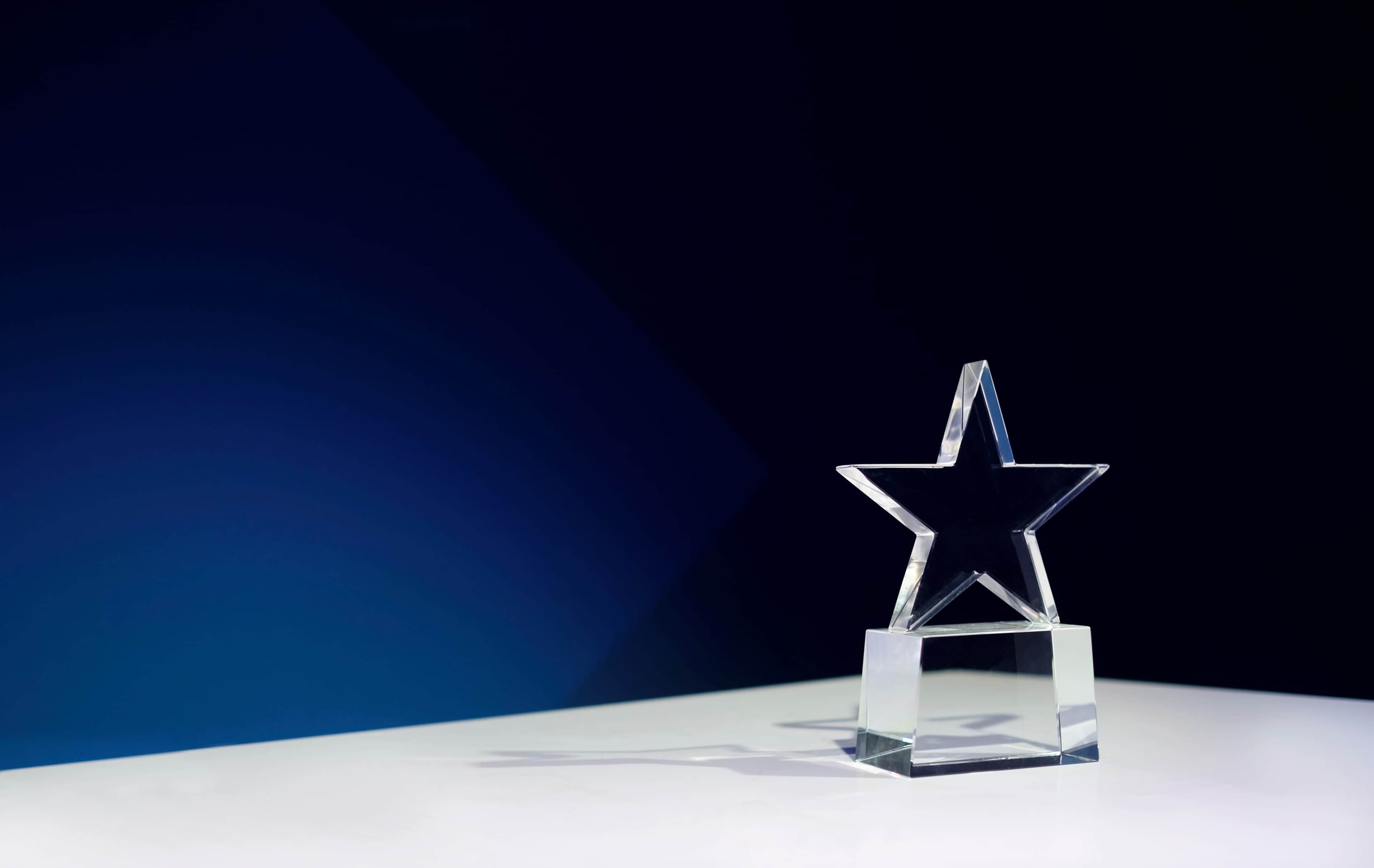 Glass star award trophy on a white table against blue background