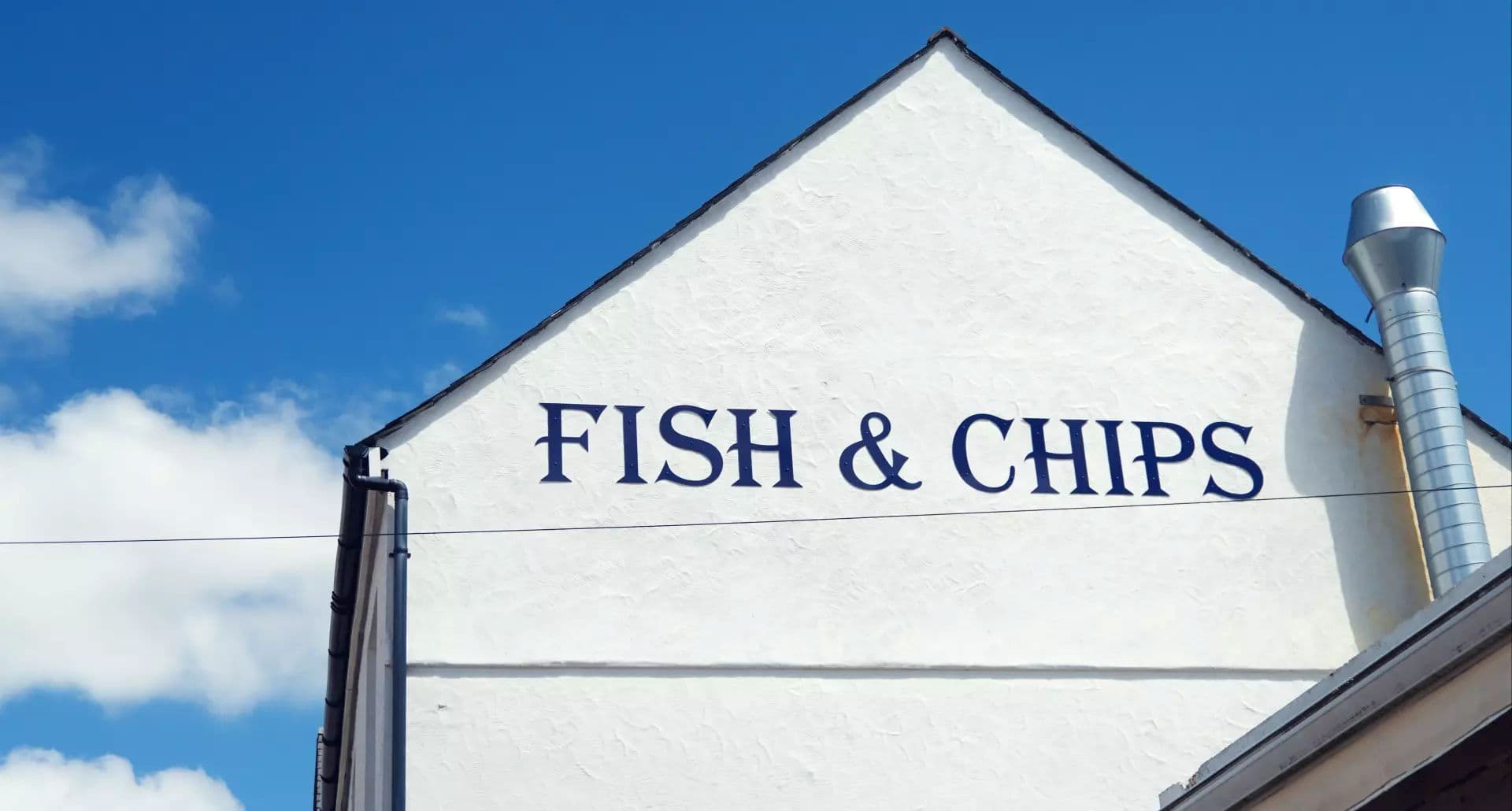 White building with fish and chips sign under blue sky