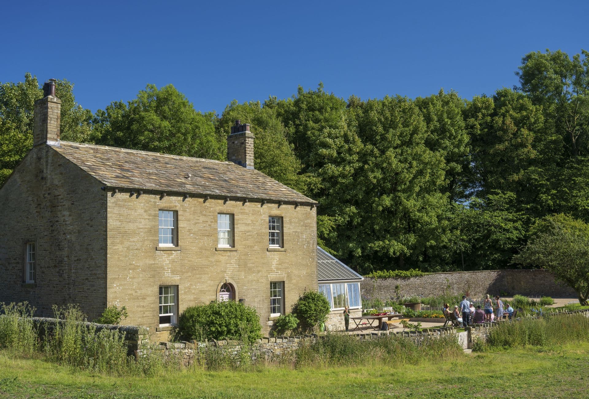 Historic stone farmhouse with people in lush garden