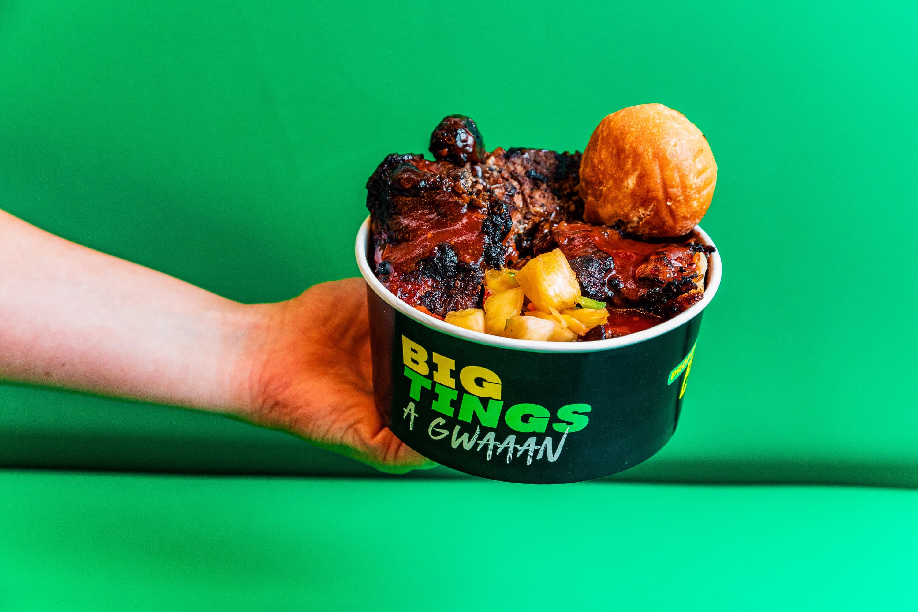 Hand holding Caribbean food bowl with grilled meats and plantains