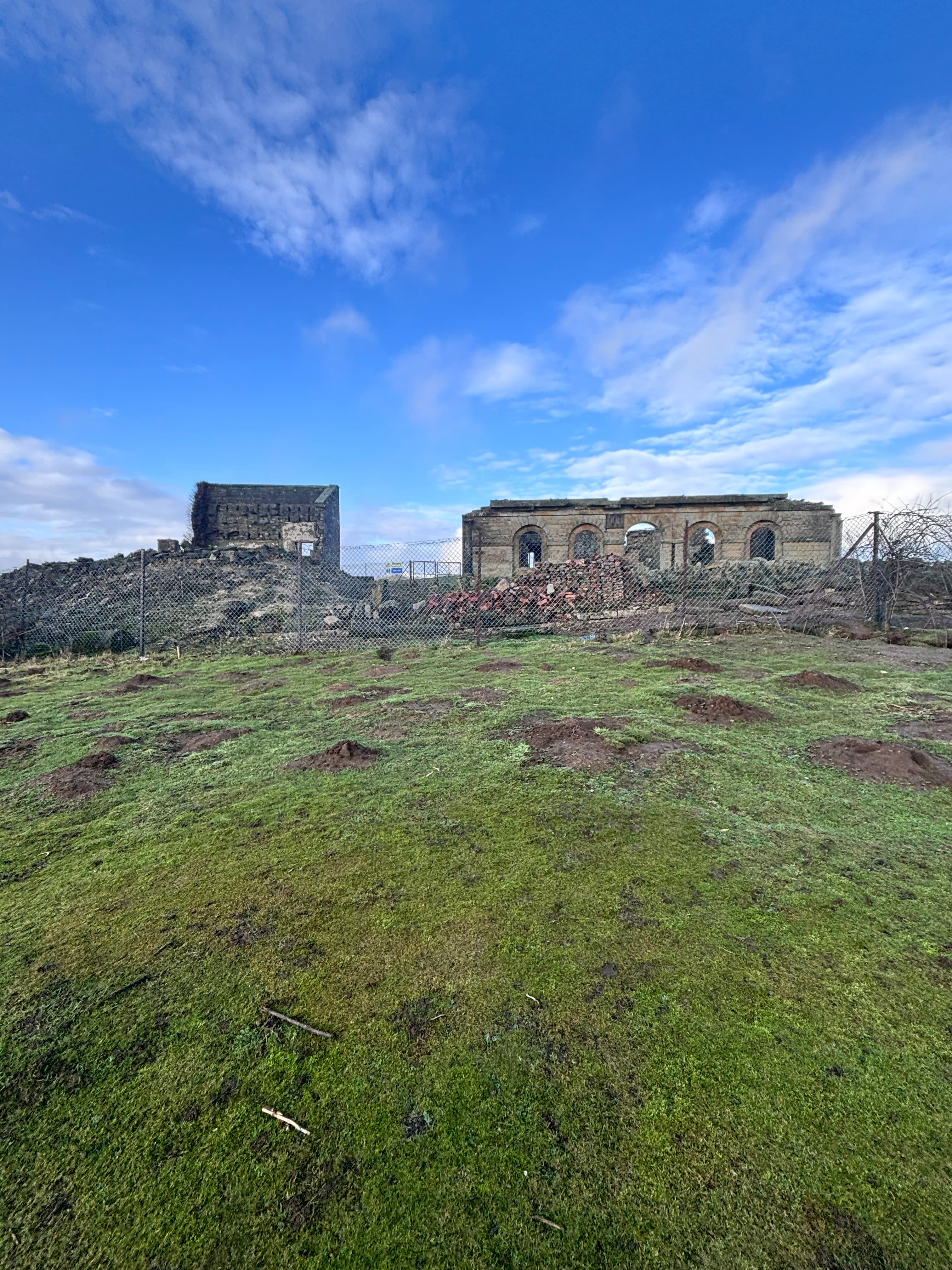 Ruins of stone buildings on a grassy hill under a blue sky