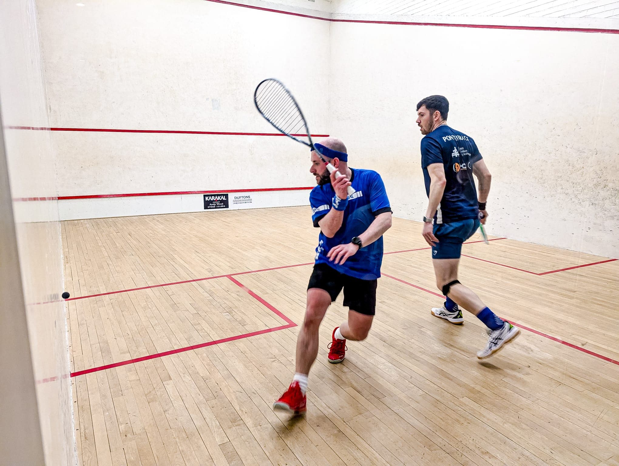 Two men playing squash in an indoor court