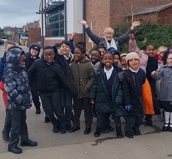 Group of smiling children and teacher outside school building