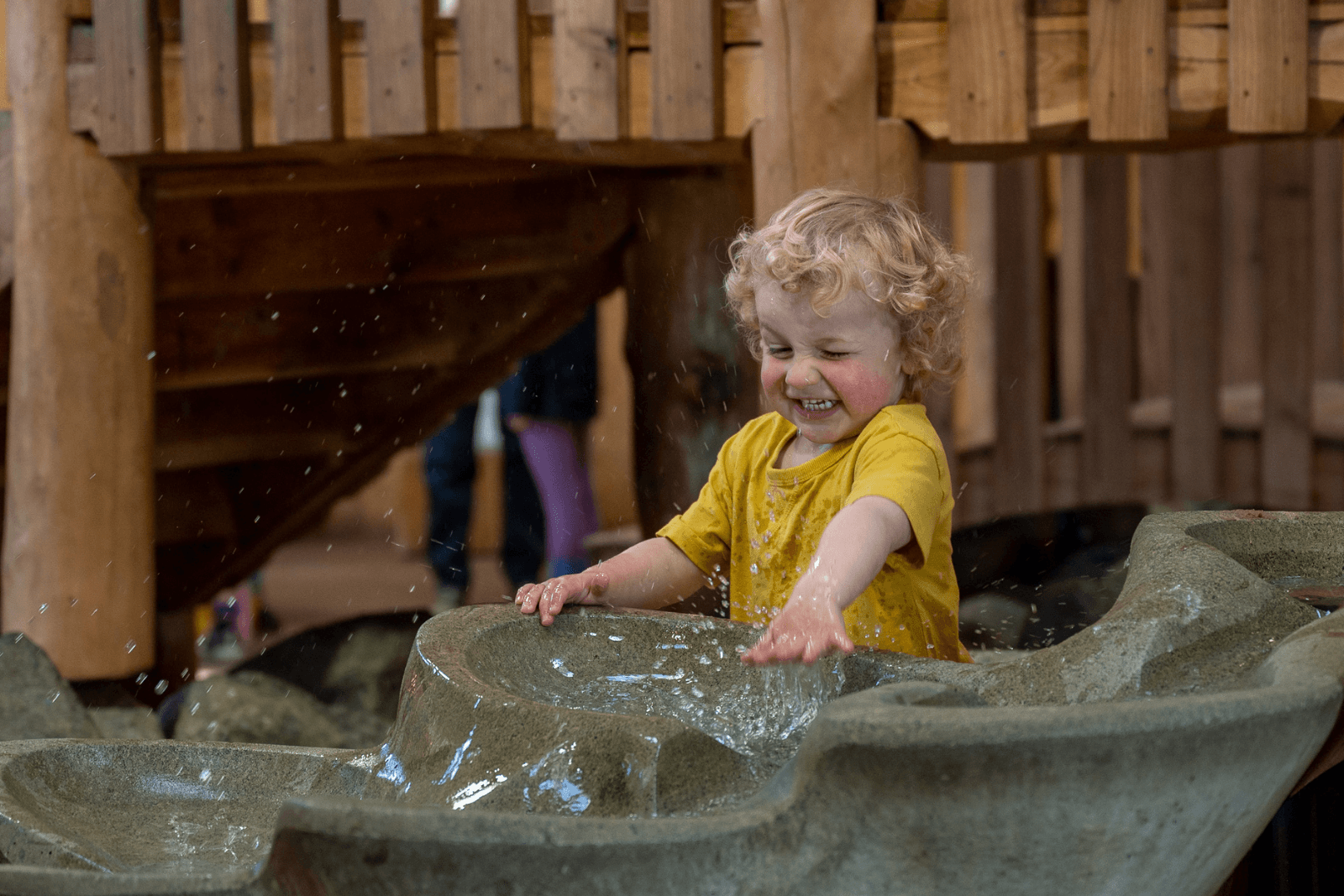Smiling child in yellow shirt playing with water feature