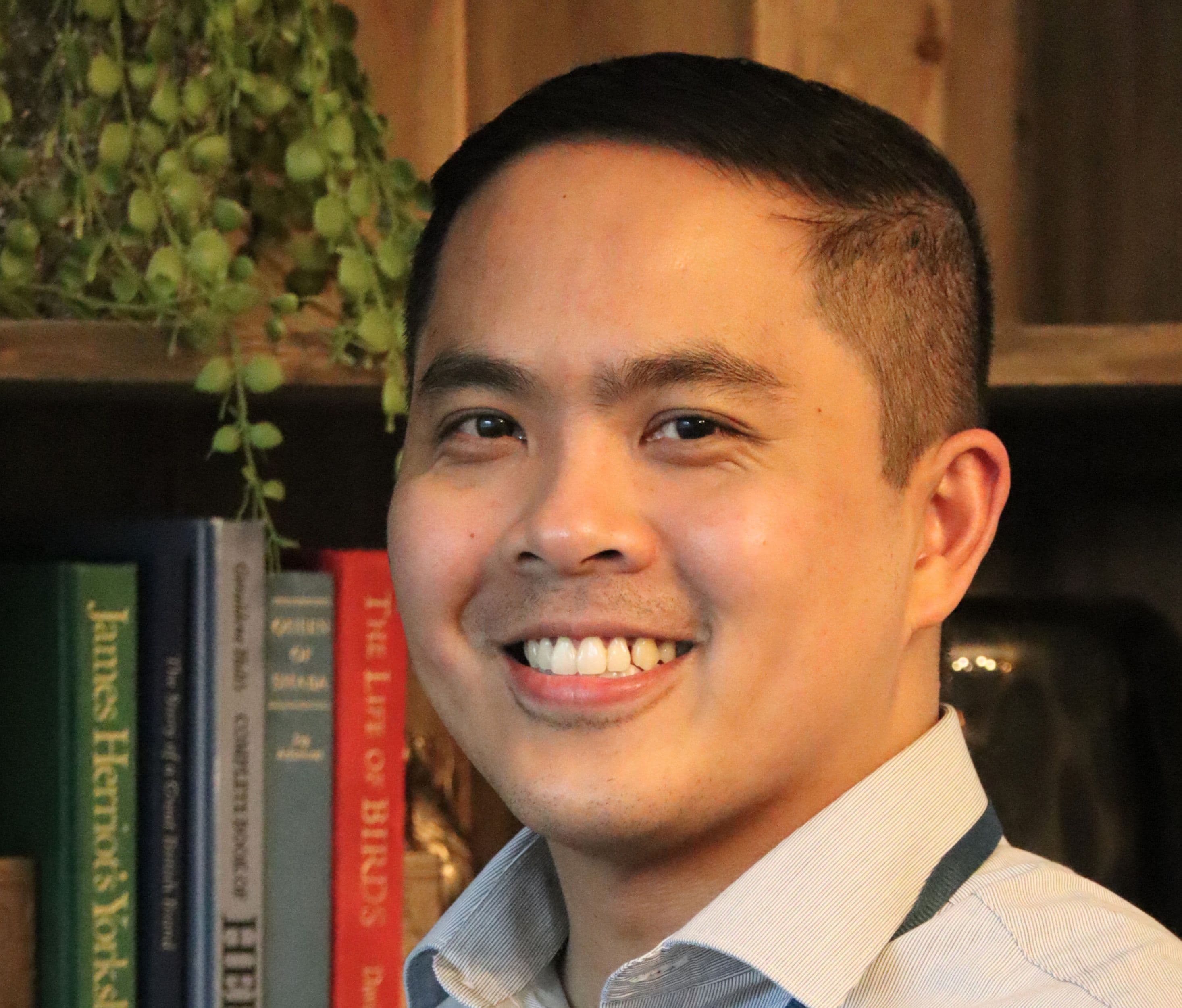 Smiling person in front of a bookshelf with green plant