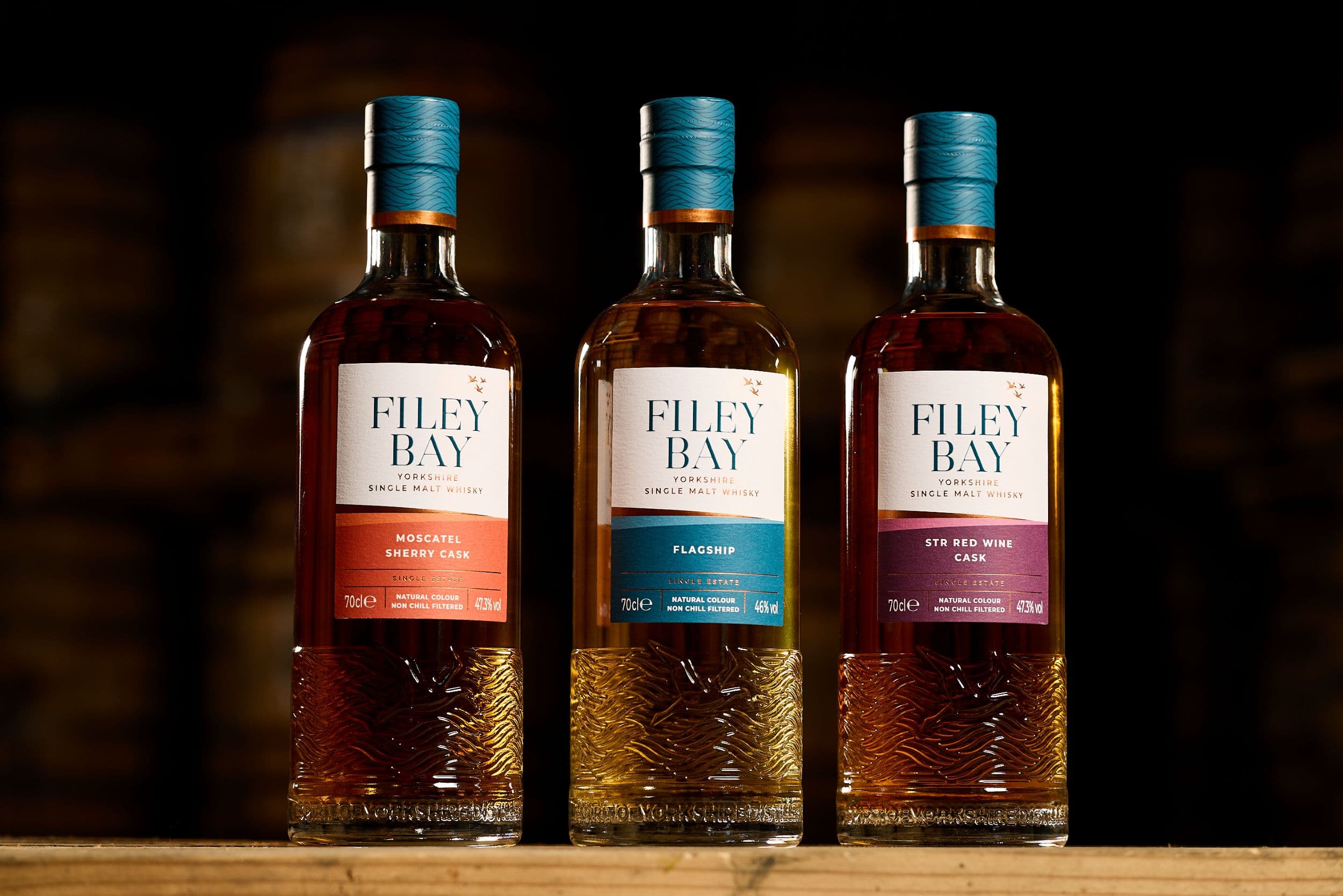 Three bottles of Filey Bay whisky on a wooden surface