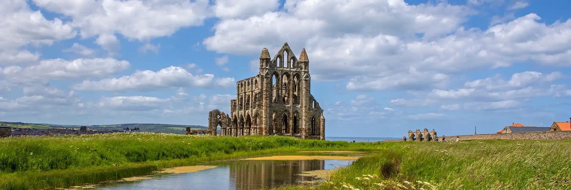 Whitby Abbey ruins under a blue sky with clouds and grassy field