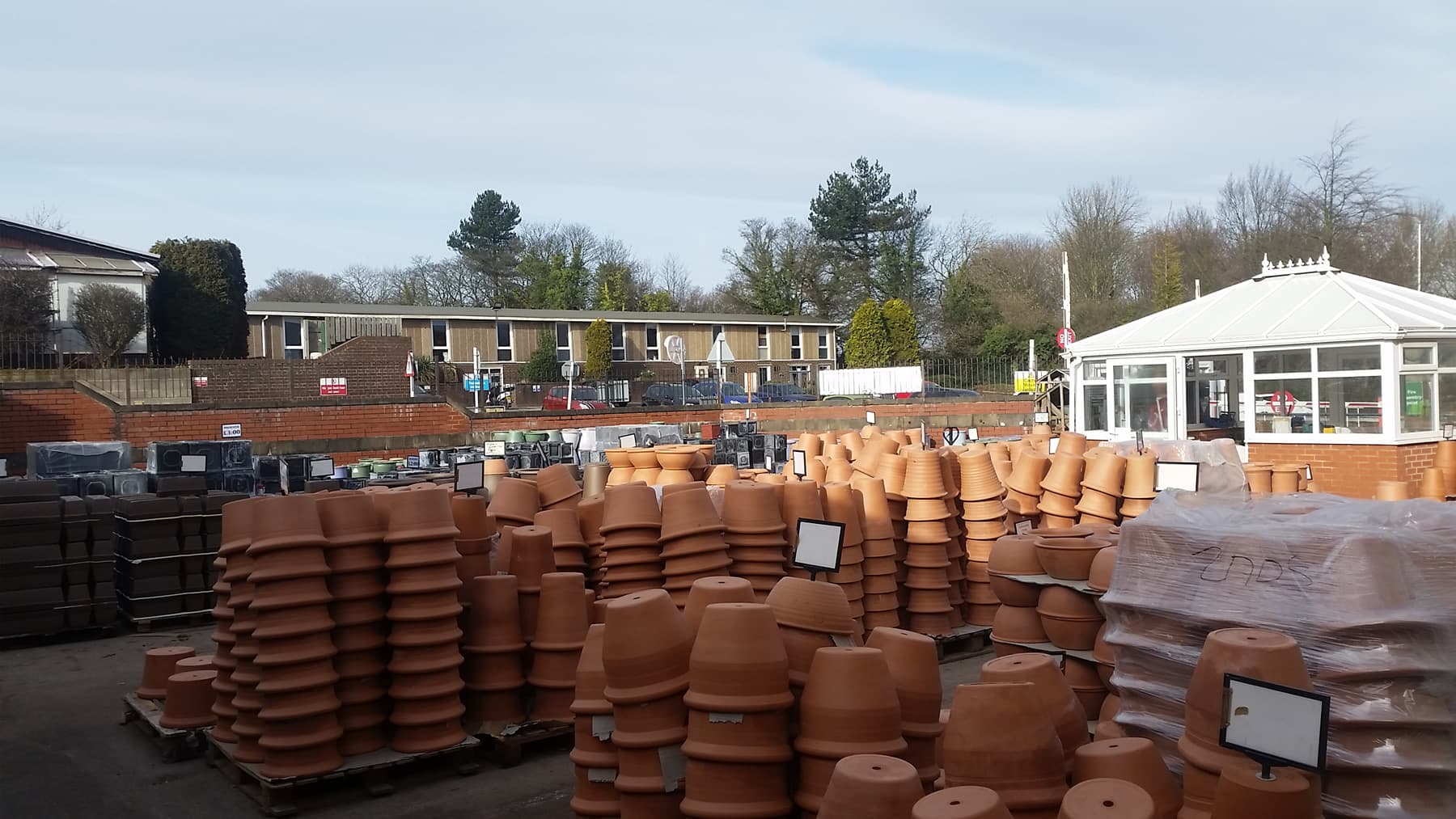 Stacks of terracotta pots in an outdoor yard with a white conservatory and trees in the background.
