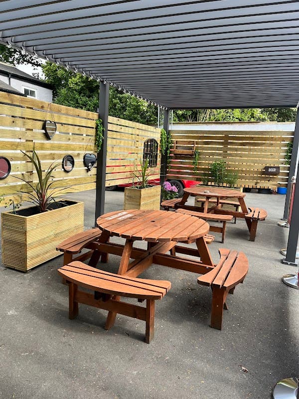 Outdoor seating area with wooden picnic tables, planters, and a wooden fence in a bar setting.