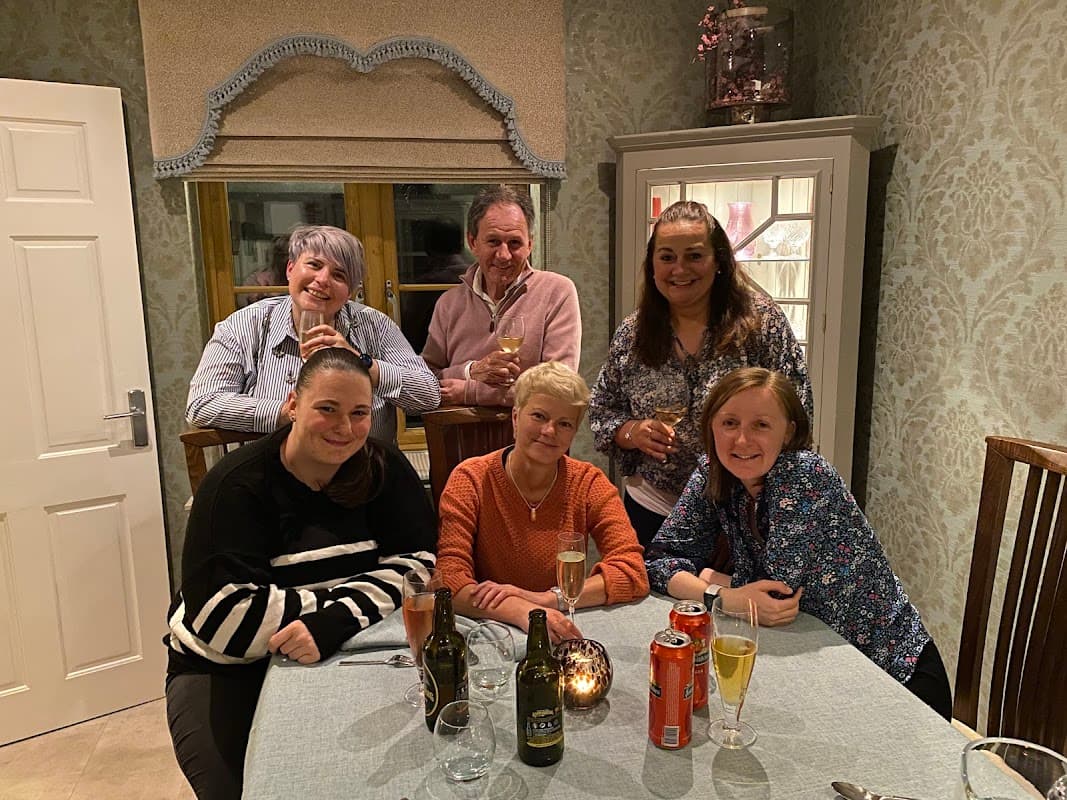 Group of six people smiling at a table with drinks, in a cozy, well-decorated indoor setting.