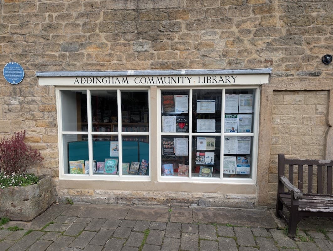 Addingham Community Library's stone exterior features large windows displaying books and community notices.