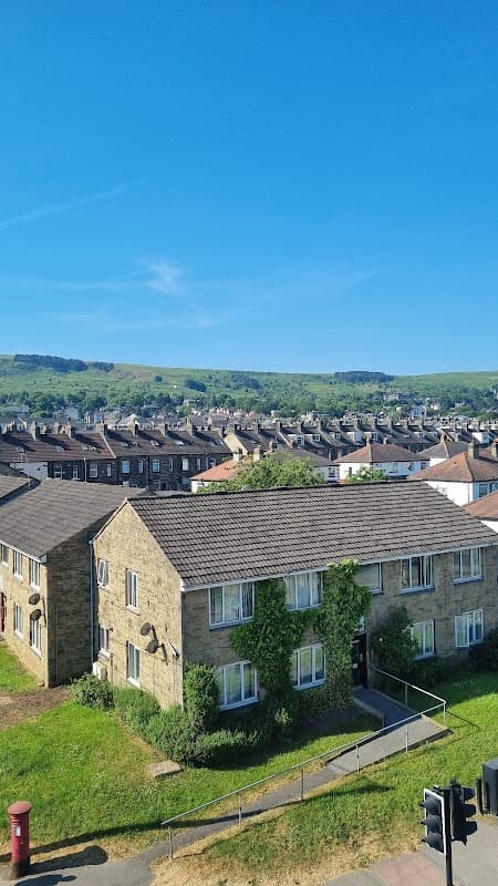 Addingham Memorial Hall with stone facade, green lawn, and blue sky, surrounded by residential buildings and hills.