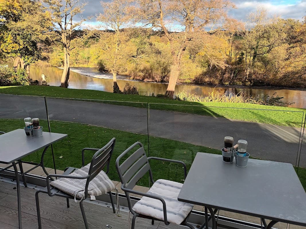 Outdoor seating at Hamiltons Cafe/Bistro overlooks a scenic river and autumn foliage in Addingham, Yorkshire.