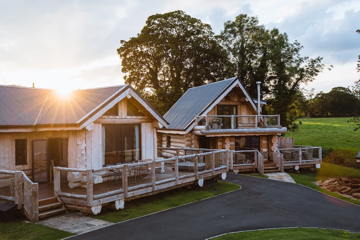 Two wooden cabins with balconies, surrounded by greenery, under a sunset sky at Olicana Park, Addingham, Yorkshire.