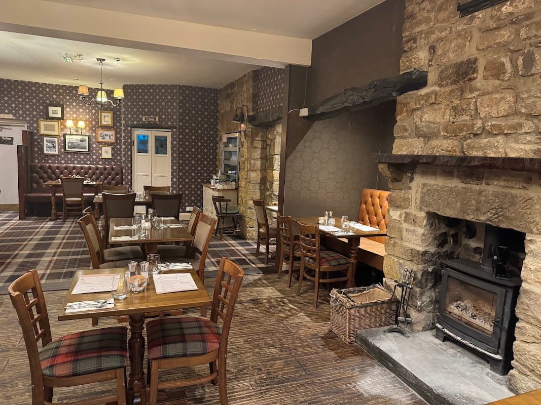 Cozy restaurant interior with wooden tables, leather seating, stone walls, and a fireplace in Addingham, Yorkshire.