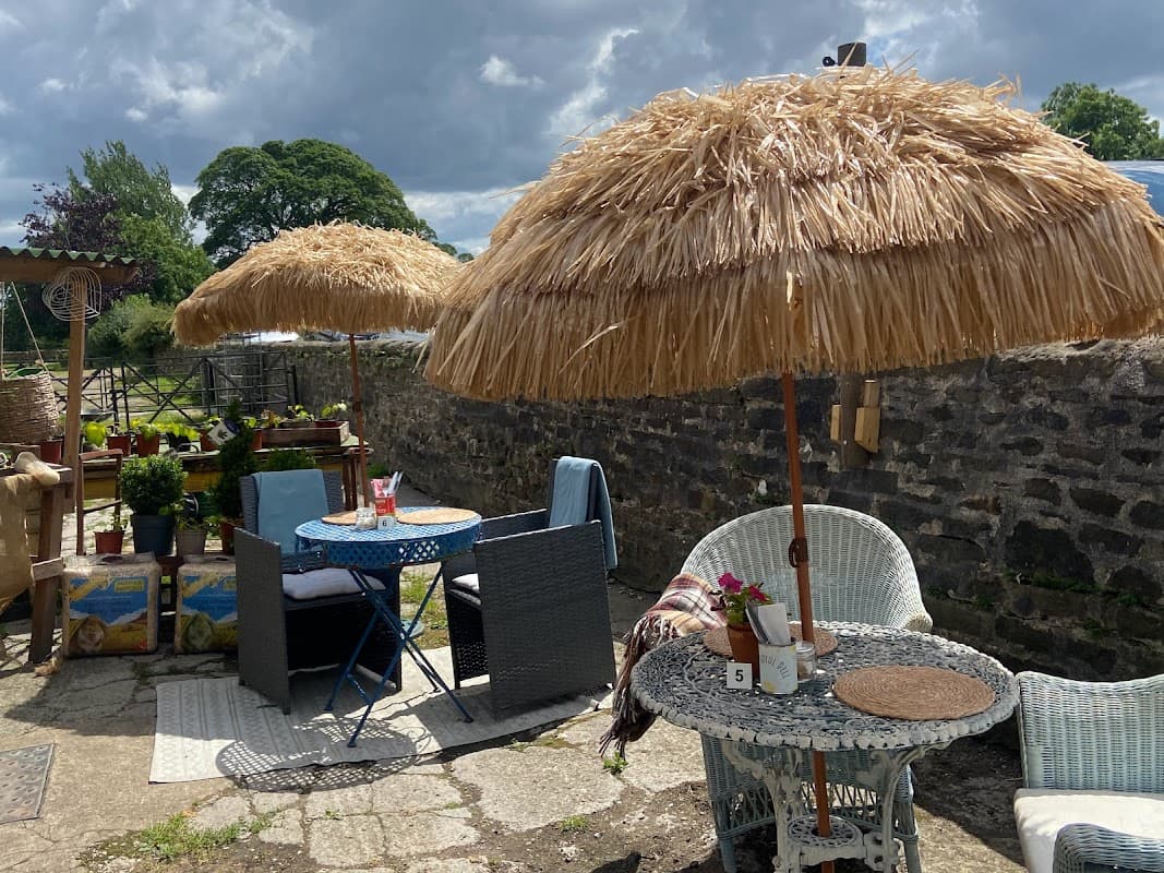 Thatched umbrellas shade outdoor seating at The Joyful Deli, surrounded by greenery and rustic stone walls.