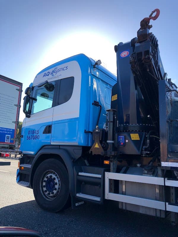 Blue and white truck with "AQ Logistics Ltd" branding, parked beside a large billboard in Ainderby Quernhow, Yorkshire.