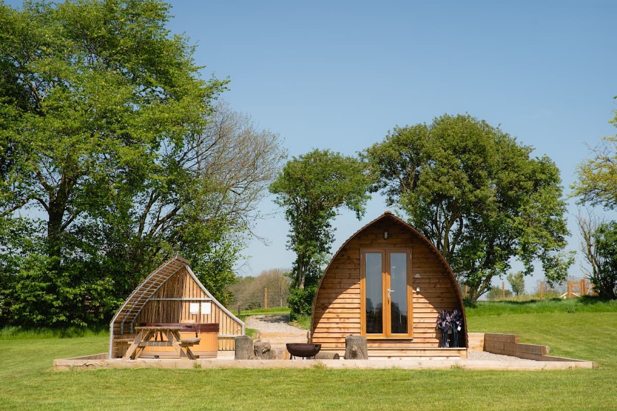 Two wooden wigwam-style cabins surrounded by green grass and trees under a clear blue sky.