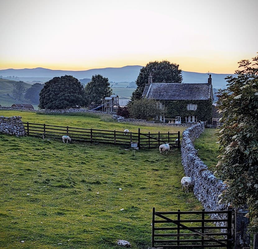 Lindon Guest House in a scenic Yorkshire landscape, with sheep grazing and hills in the background at sunset.