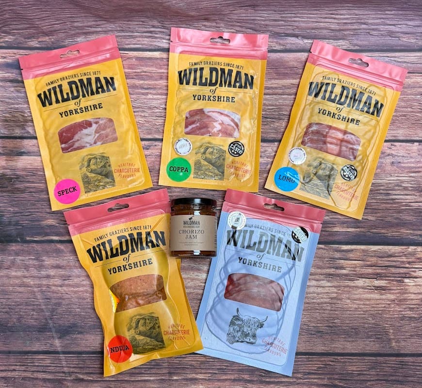 Five colorful packages of cured meats labeled "Wildman of Yorkshire," featuring speck, coppa, lomo, and chorizo.