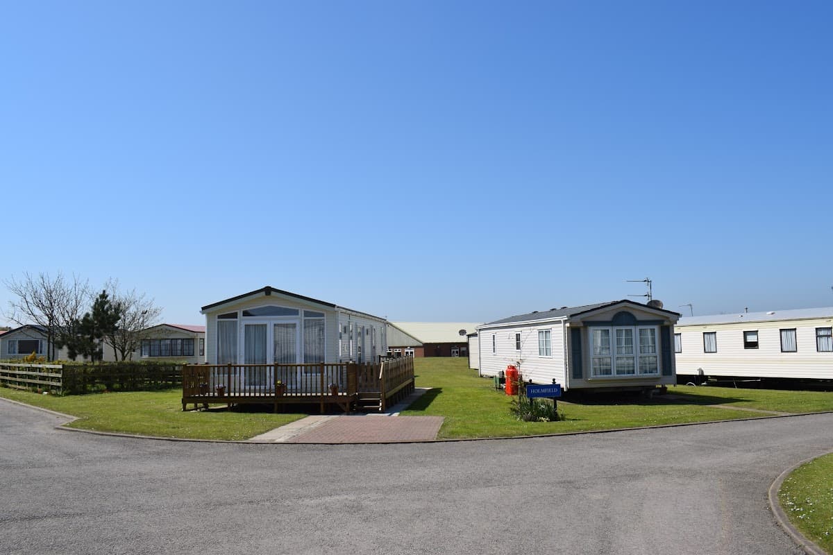 Two static caravans on a grassy area, surrounded by trees and a clear blue sky at Aldbrough Leisure Park.