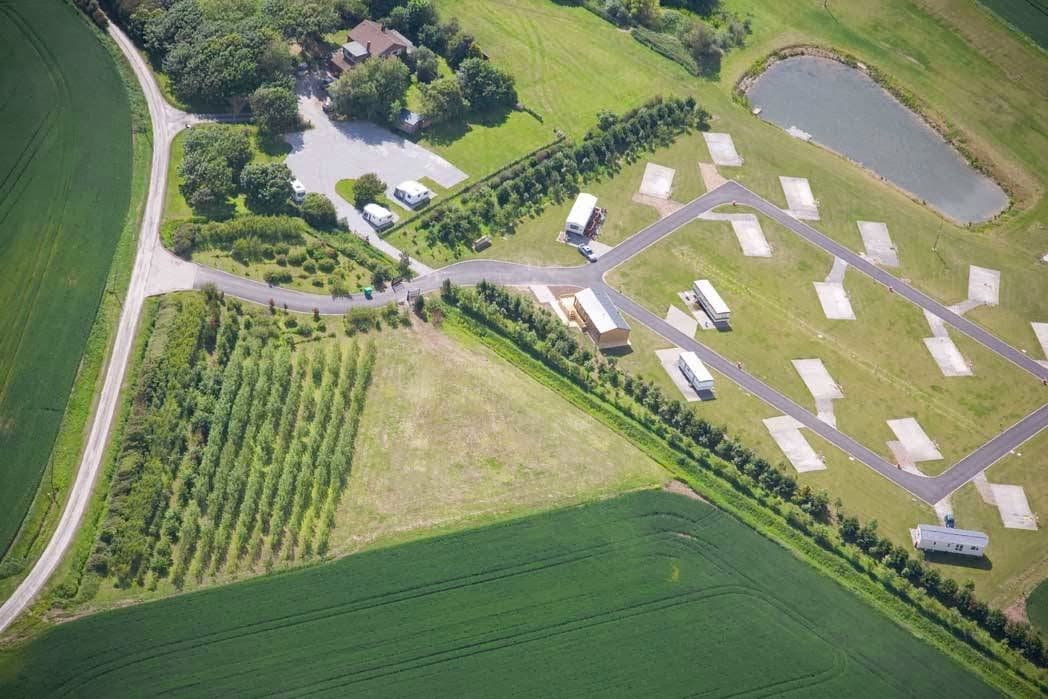 Aerial view of Newton Shores Hotel, surrounded by green fields, a pond, and neatly arranged accommodations.