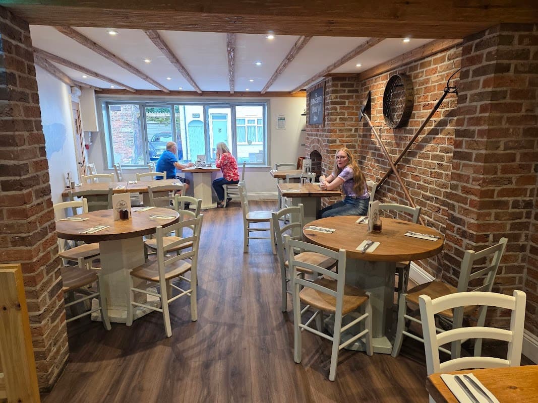 Cozy restaurant interior with wooden tables, chairs, brick walls, and customers dining by the window.