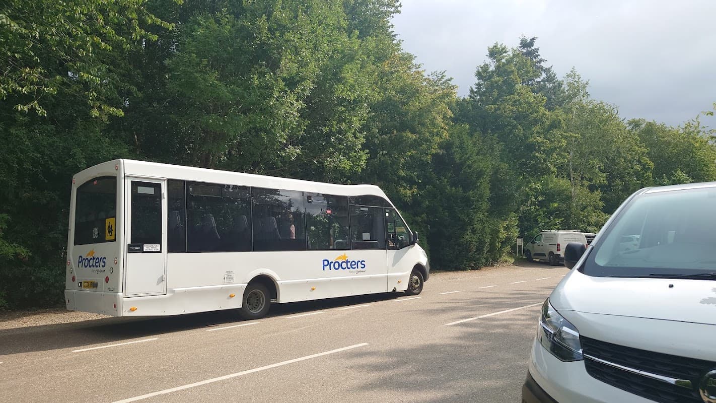 White bus with "Procters" branding parked alongside trees in a visitor center area.
