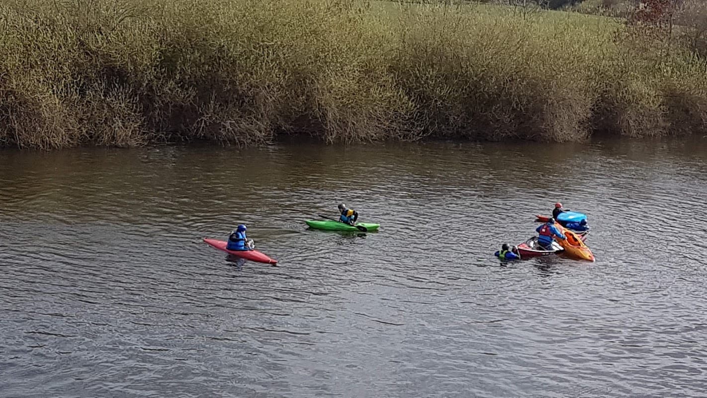 Kayakers in colorful boats paddling on a calm river surrounded by lush greenery at Aldwark Activity Centre.