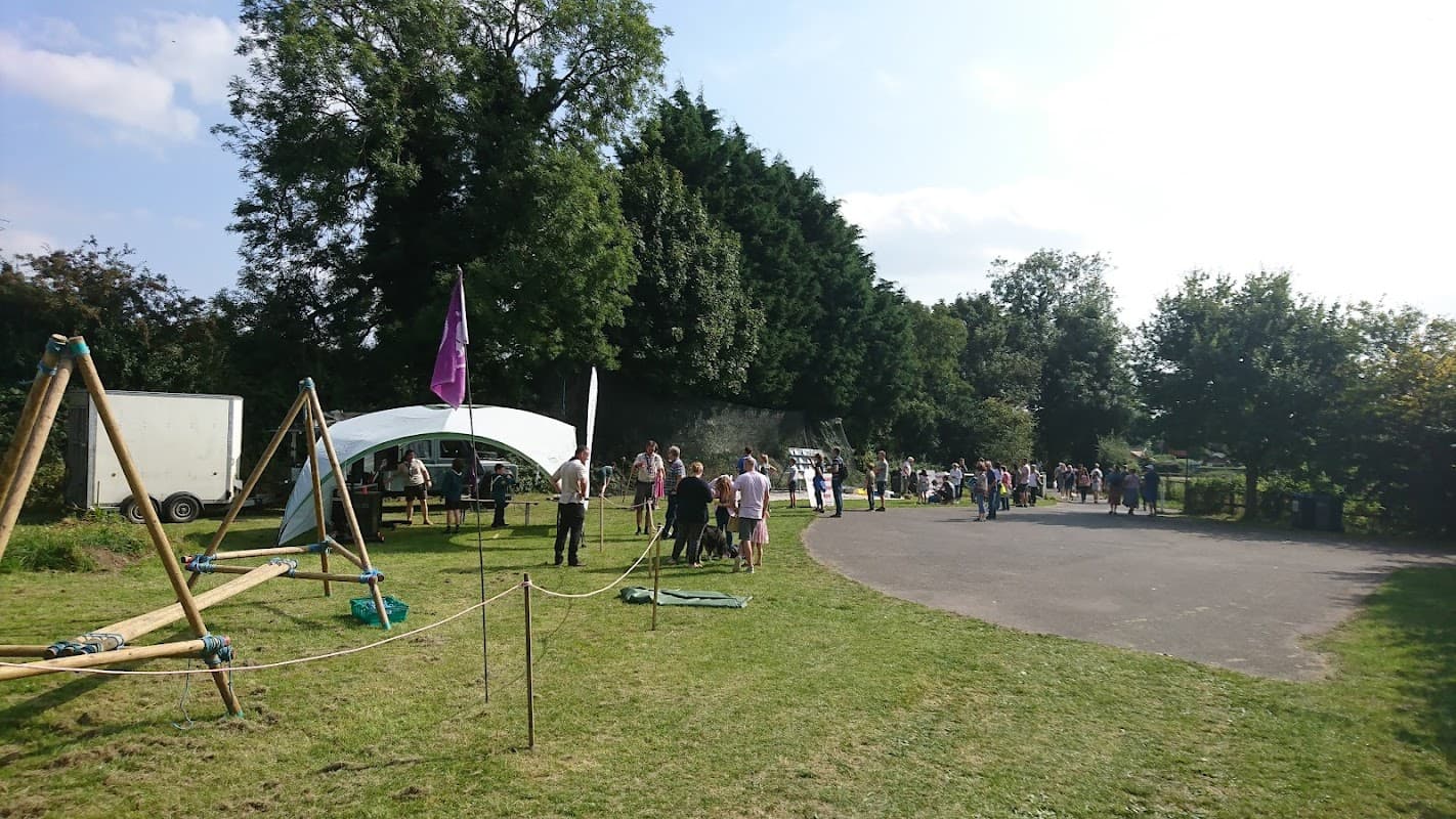 Community event at Alne Parish Leisure Association with people gathering, swings, and a tent under a sunny sky.