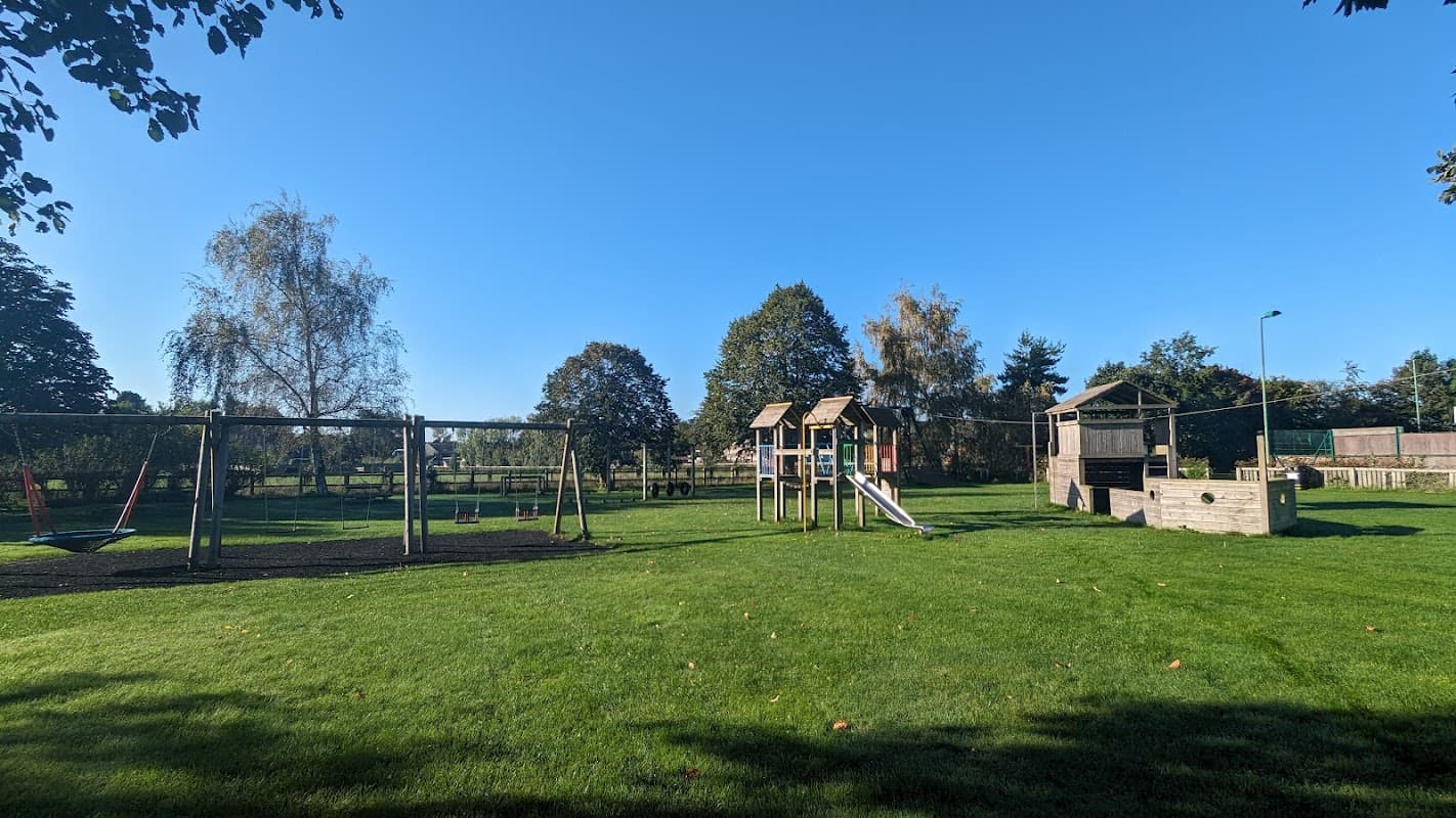 Playground with swings and climbing structures set in a grassy area under a clear blue sky in Alne, Yorkshire.