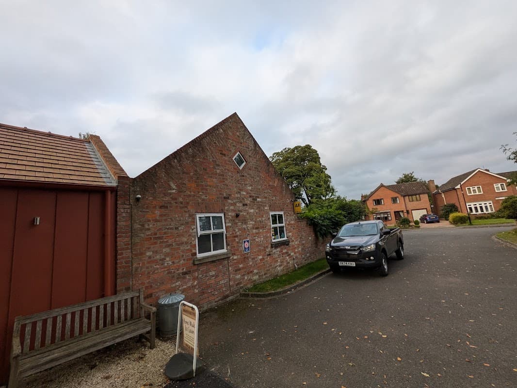 Brick building with a slanted roof, parked black vehicle, and residential homes in a quiet neighborhood.