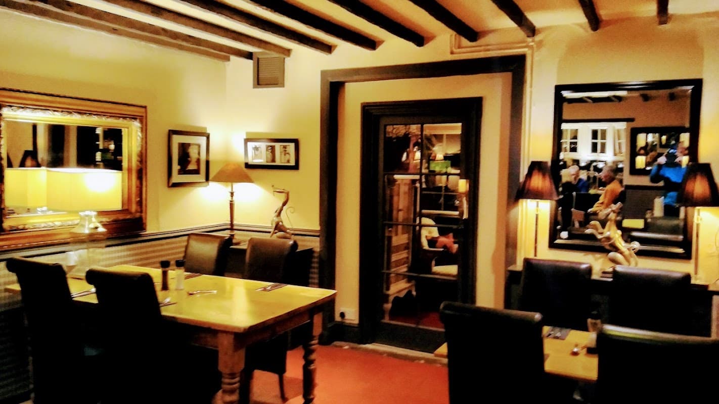 Cozy dining area with wooden beams, tables, and elegant lamps, featuring a mirror and framed artwork on the walls.