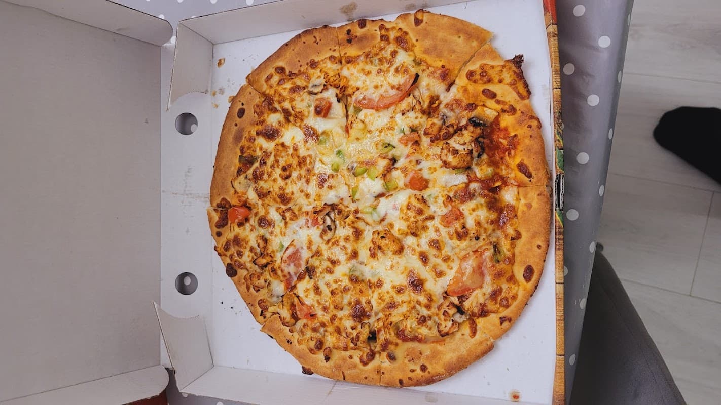 A pizza with melted cheese, tomatoes, and green peppers in a pizza box, resting on a polka dot tablecloth.