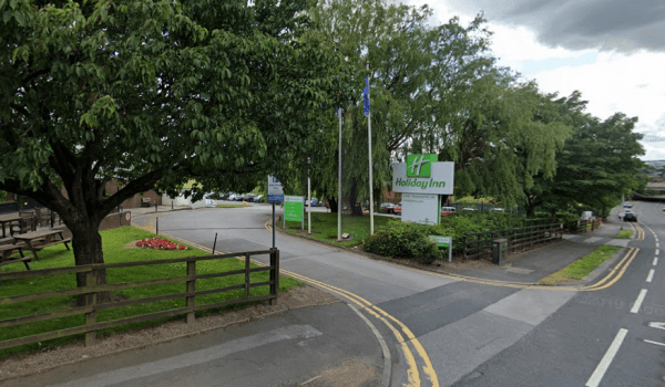 Entrance to Holiday Inn with green signage, trees, and parked cars along a quiet road in Alverthorpe, Yorkshire.