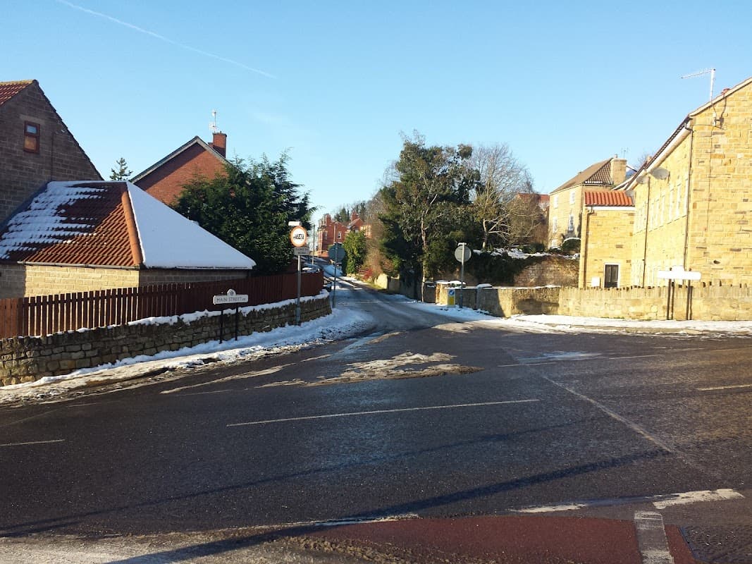 Quiet street in Anston, Yorkshire, with snow on the ground, lined by houses and trees under a clear blue sky.