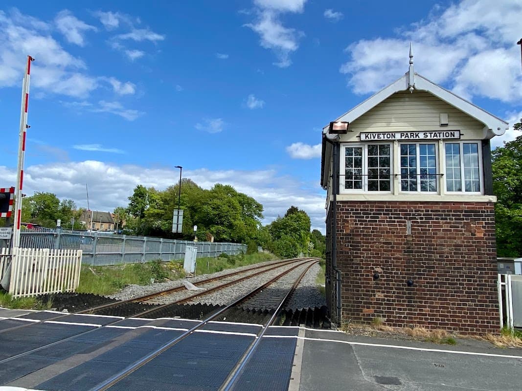 Kiveton Park Station building beside railway tracks, with blue sky and greenery in the background.