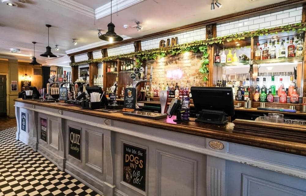 A stylish bar with a wooden counter, colorful liquor bottles, and a checkered floor in a cozy setting.