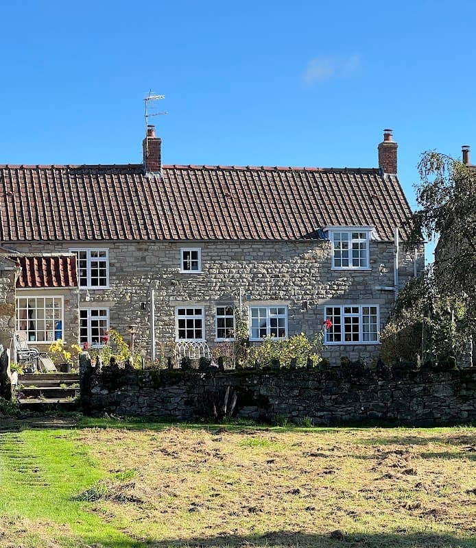 Charming stone farmhouse with a red-tiled roof, surrounded by greenery and a stone wall, under a clear blue sky.