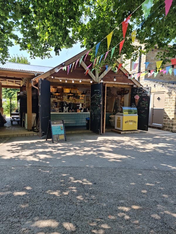 Campsite shop with colorful bunting, outdoor seating, and a menu board under leafy trees in Appletreewick, Yorkshire.