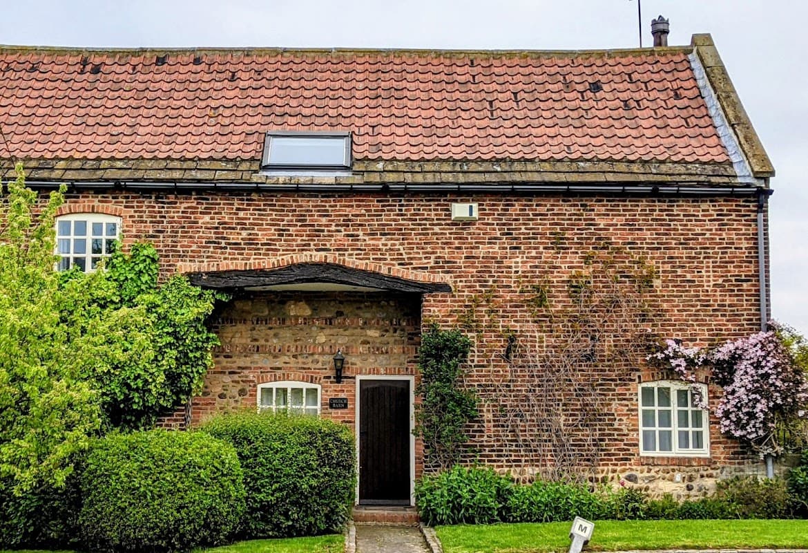 Community hall with a brick facade, a red-tiled roof, and greenery surrounding the entrance in Arkendale, Yorkshire.