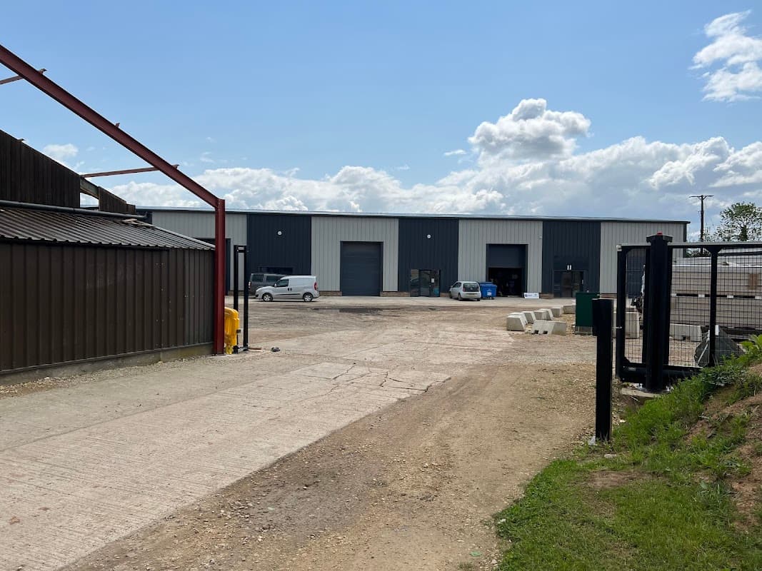 Business park with industrial buildings, parked vehicles, gravel driveway, and partly cloudy sky in Asenby, Yorkshire.