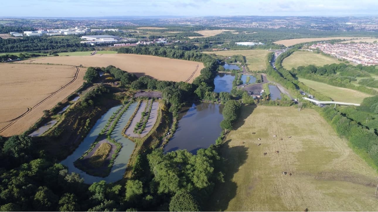 Aston Park Fisheries features multiple ponds surrounded by greenery and fields, with distant hills and a rural landscape.