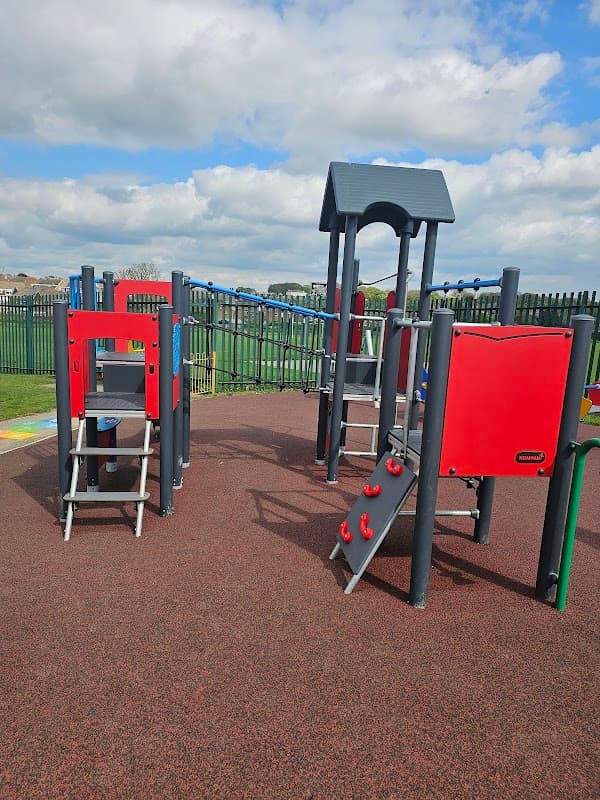 Colorful playground equipment with slides and climbing structures on a rubber surface under a partly cloudy sky.