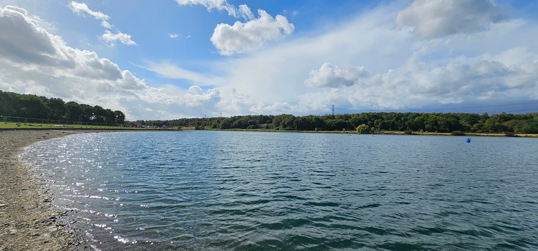 Serene lake with shimmering water, surrounded by trees and a clear sky, near the Rother Valley Watersports Centre.