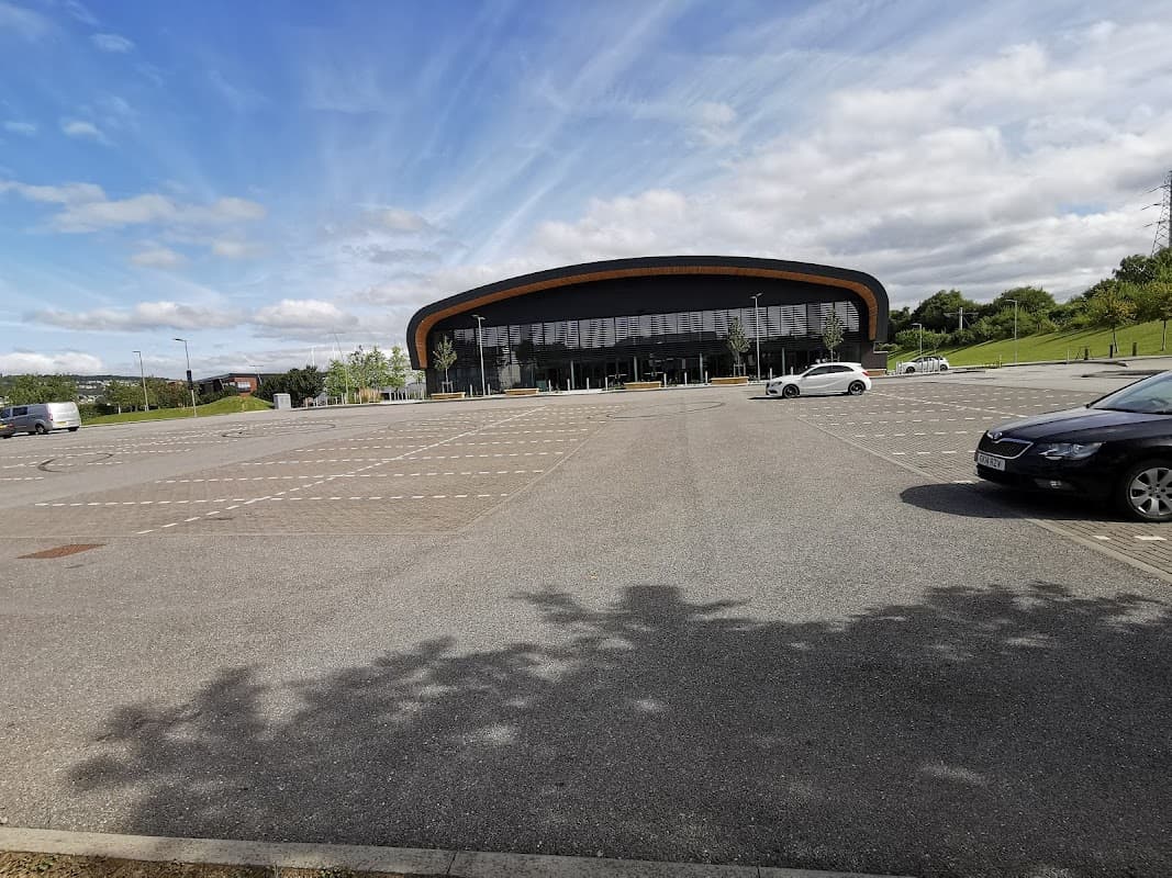 Spacious car park at Sheffield Olympic Legacy Park, featuring a modern building and clear blue skies.