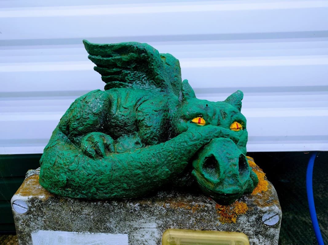 A green dragon statue with wings and glowing orange eyes resting on a stone pedestal at Barcourt Estate Caravan Park.